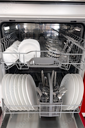 Clean dishes are piled into a household kitchen dishwasher.