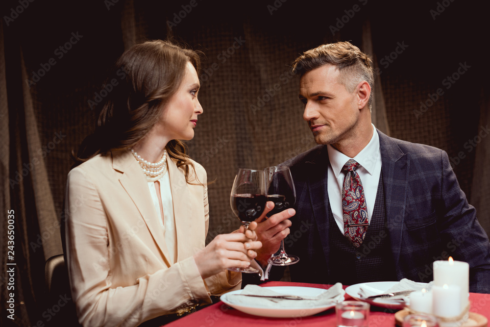 couple sitting at table and clinking glasses of red wine during romantic date in restaurant couple sitting at table and clinking glasses of red wine during romantic date in restaurant