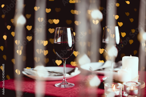 selective focus of red wine glasses with heart shaped bokeh on background
