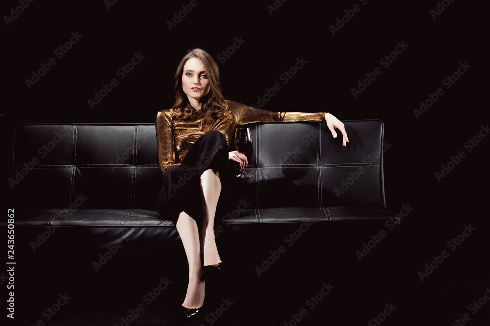 beautiful glamorous woman sitting on couch with glass of red wine isolated on black