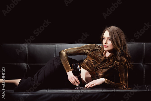 beautiful elegant woman lying on couch with glass of red wine isolated on black