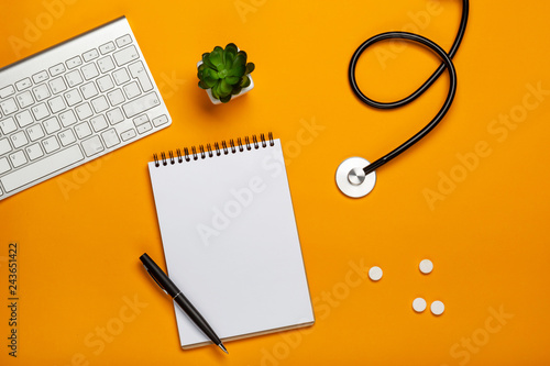 Top view of doctor's desk with stethoscope keyboard notepad and pen, prescription and pills