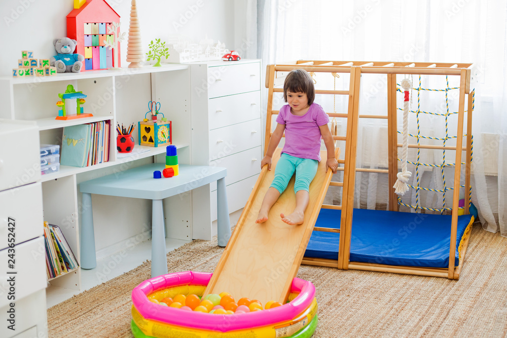 Obraz premium little girl having fun riding a roller coaster on a wooden home sports gaming complex stairs, rings and rope.