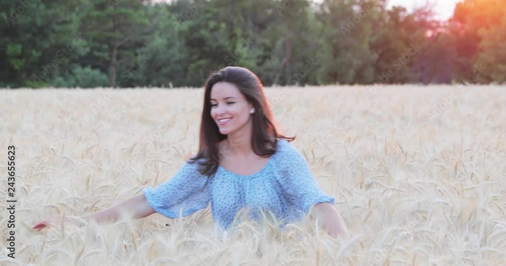 The beautiful young girl with long brunette hairs poses in the field with wheat, sunset light, turns, smiles, flirts, happy, blue dress, France, Provence The beautiful young girl with long brunette hairs poses in the field with wheat, sunset light, turns, smiles, flirts, happy, blue dress, France, Provence