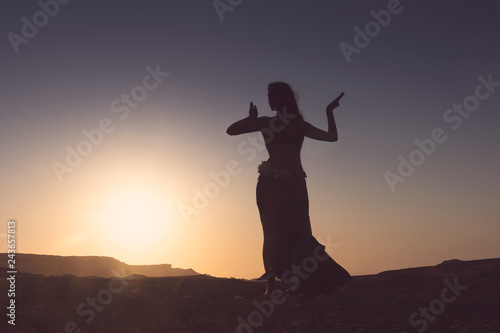 Woman dancing to the famous Arab belly dance. With sunset in the arid desert plain of Namibe. Africa. Angola. photo