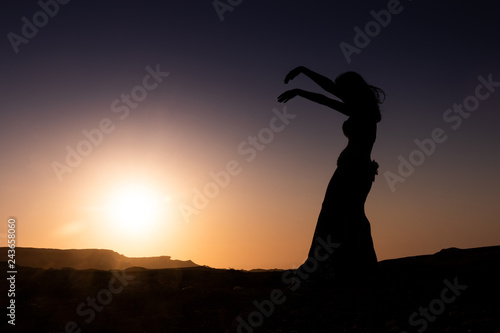 Woman dancing to the famous Arab belly dance. With sunset in the arid desert plain of Namibe. Africa. Angola. photo