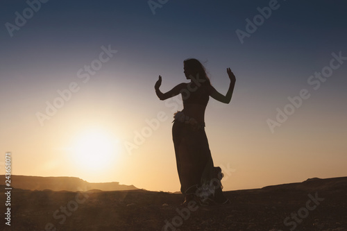 Woman dancing to the famous Arab belly dance. With sunset in the arid desert plain of Namibe. Africa. Angola.