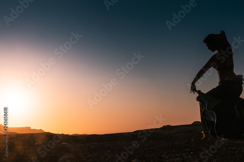 Woman dancing to the famous Arab belly dance. With sunset in the arid desert plain of Namibe. Africa. Angola. photo