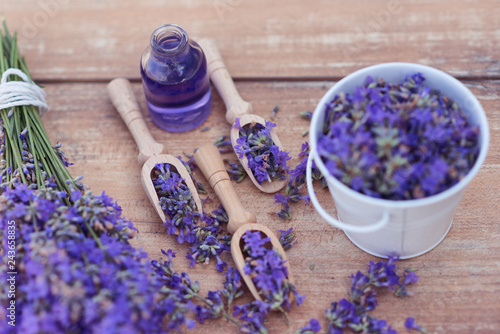 Fototapeta Naklejka Na Ścianę i Meble -  Top view of a bowl and wooden spoons with fresh lavender flowers, lavender essential oil and a bouquet of lavender on a brown wooden background.