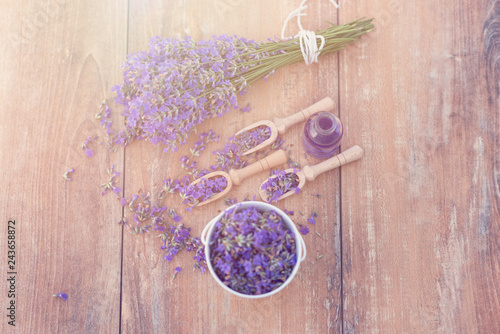 Top view of a bowl and wooden spoons with fresh lavender flowers and a bouquet of lavender on a brown wooden background.