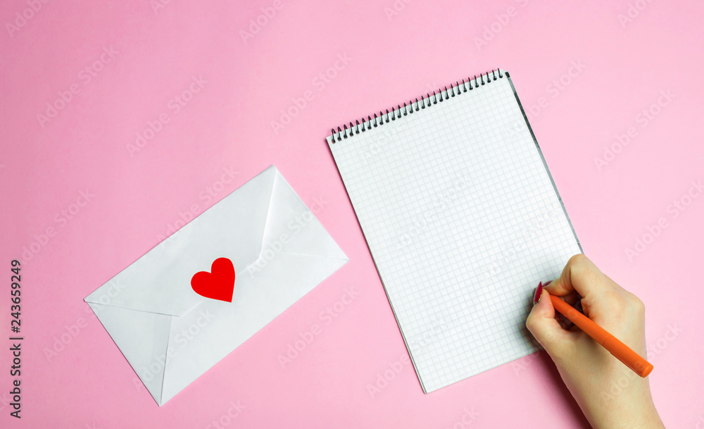 Female hand writing a love letter. Valentines day concept. Greeting valentine card. Declaration of love. Wedding invitation. Red heart. Pink background. View from above. Flat lay Female hand writing a love letter. Valentines day concept. Greeting valentine card. Declaration of love. Wedding invitation. Red heart. Pink background. View from above. Flat lay
