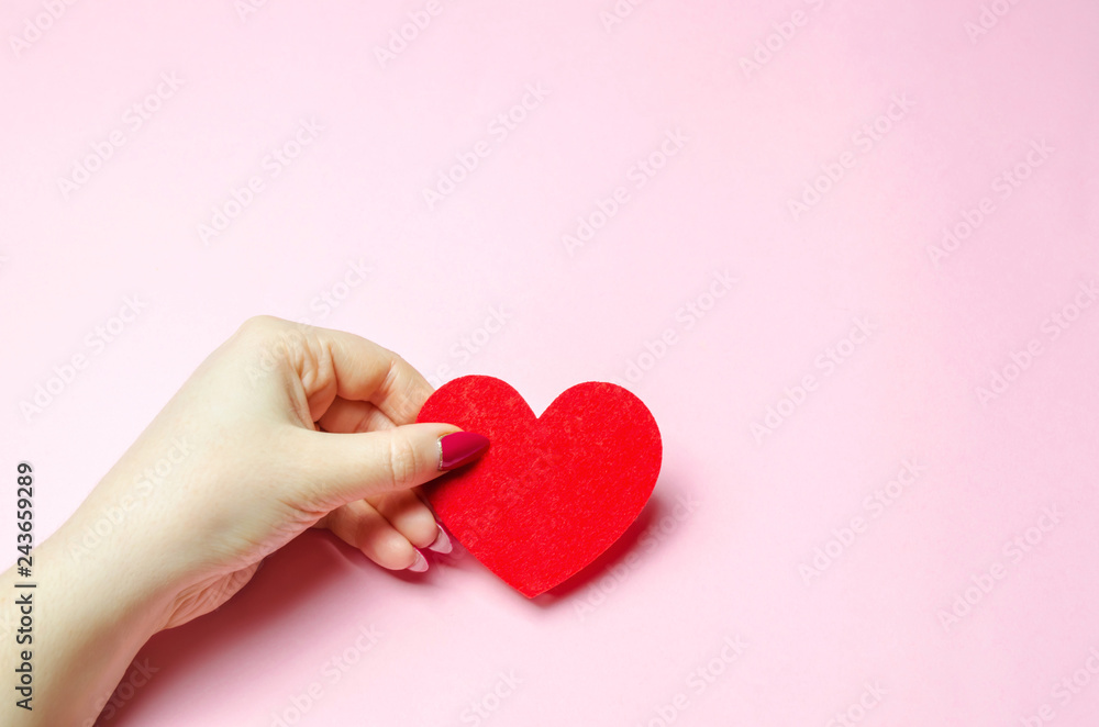 The girl holds a red heart in hands. Valentine's day concept. Love and romance. Holiday. Minimalism. Romantic composition. Health and life insurance. Place for text. Flat lay. Pink background