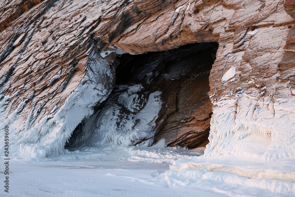 Obraz premium Cave entrance in textured and snow-covered rocks, view from outside, scenic winter landscape or background