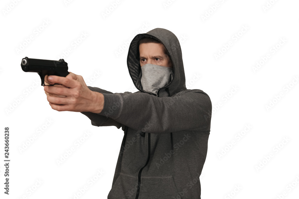 The man in a sports gray jacket and in a mask on a face shoots with the gun. White background The man in a sports gray jacket and in a mask on a face shoots with the gun. White background