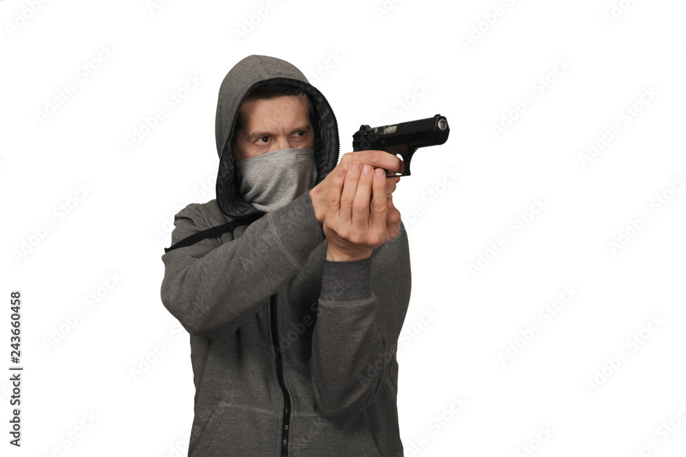 The man in a sports gray jacket and in a mask on a face shoots with the gun. White background The man in a sports gray jacket and in a mask on a face shoots with the gun. White background
