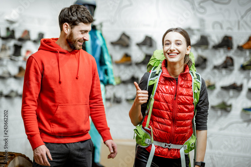 Fototapeta Naklejka Na Ścianę i Meble -  Salesman selling travel equipment to a young woman client trying a backpack in the sports shop