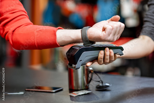 Man using handwatch on the cash register for buying goods at the sports shop, close-up view with no face photo