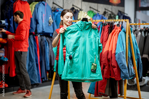 Young woman choosing winter clothes trying windbreaking jacket in the sports shop