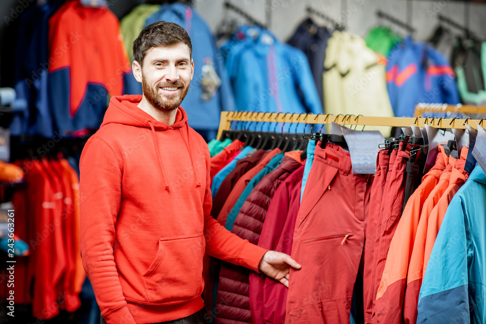 Portrait of a handsome man standing as a seller or customer in the clothing department with jackets in a sports shop