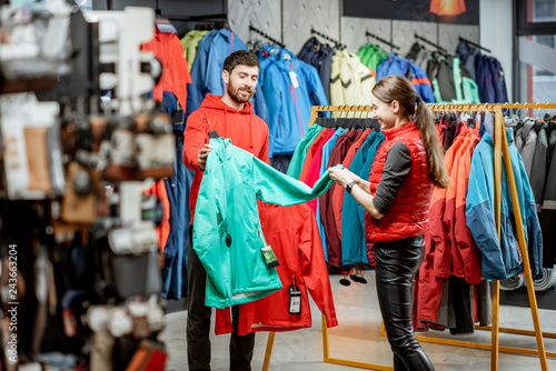 Cheerful couple choosing color of the windbraking jacket shopping together in the sports shop