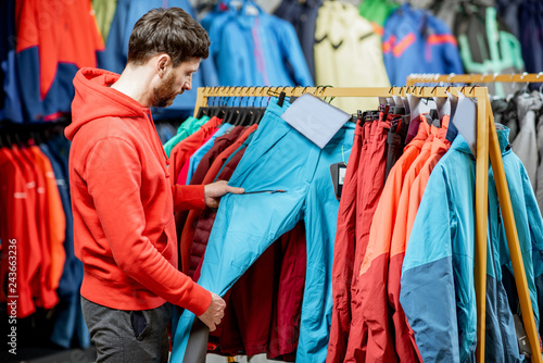 Man choosing winter clothes picking up trousers on the hanger in the sports shop