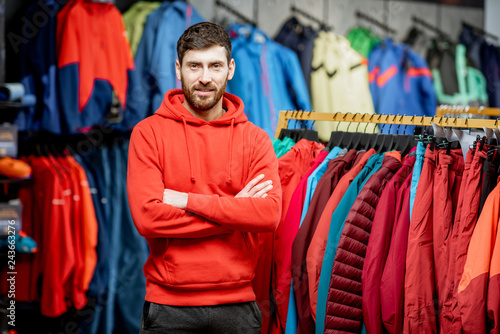 Portrait of a handsome man standing as a seller or customer in the clothing department with jackets in a sports shop photo