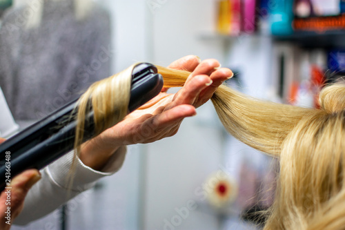 Close-up photo professional hairdresser uses flat iron for making curls on beautiful blonde hair