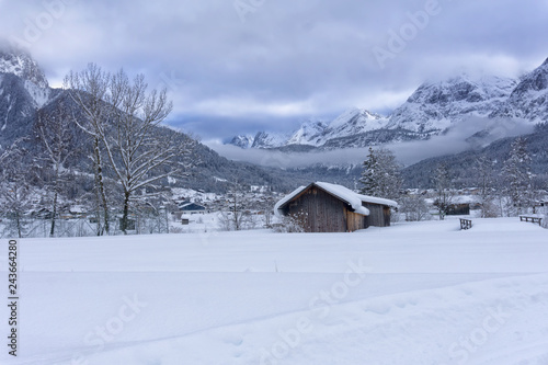 Winter mountain landscape with a wooden shed in the foreground. Cloudy weather and fog are falling in the valley. Ehrwald, Austria, Europe.