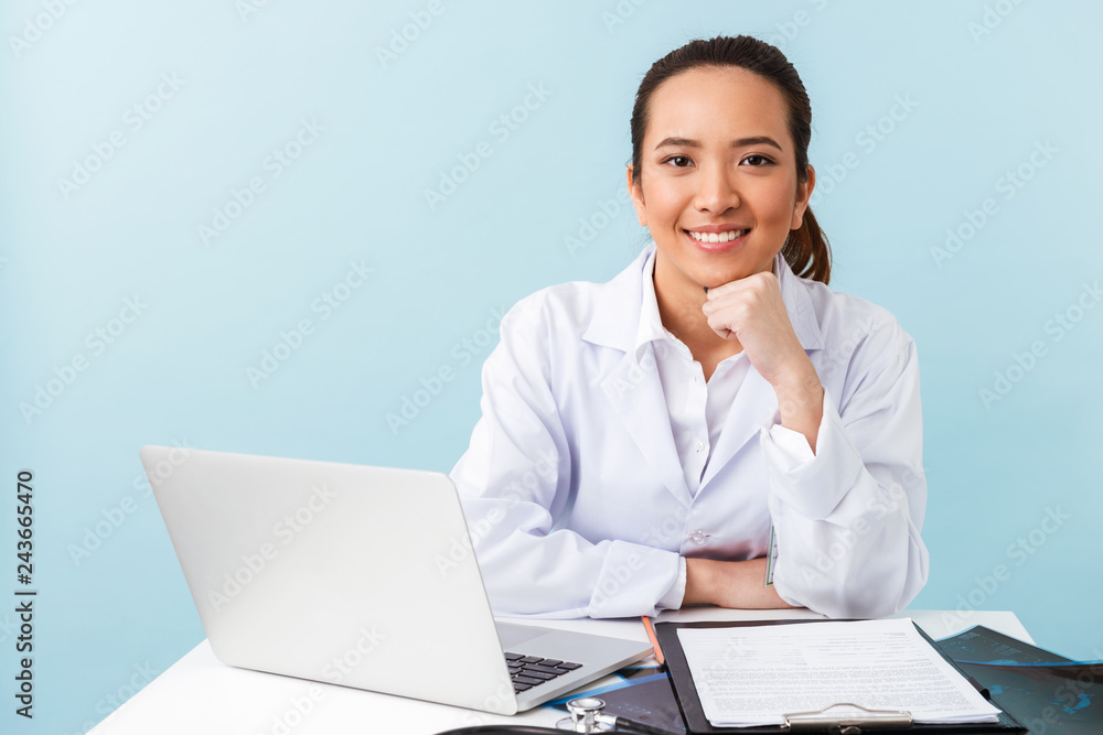 Woman doctor posing isolated over blue wall background using laptop computer. Woman doctor posing isolated over blue wall background using laptop computer.