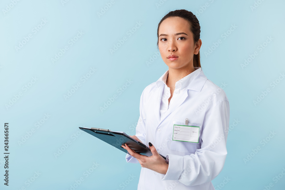 Woman doctor posing isolated over blue wall background holding clipboard.