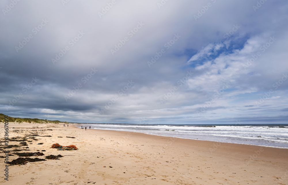 DRURIDGE BAY, ENGLAND, UK - JUNE 03, 2016: People walking along the golden sands of Druridge Bay in Northumberland, England. DRURIDGE BAY, ENGLAND, UK - JUNE 03, 2016: People walking along the golden sands of Druridge Bay in Northumberland, England.