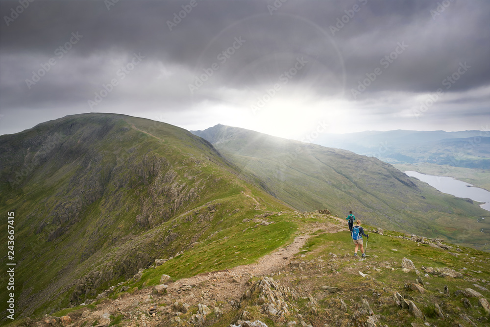 Two hikers walking along Swirl Band towards the summit of the Old Man of Coniston in the English Lake District.