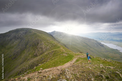 Obraz na płótnie Two hikers walking along Swirl Band towards the summit of the Old Man of Coniston in the English Lake District. w salonie
