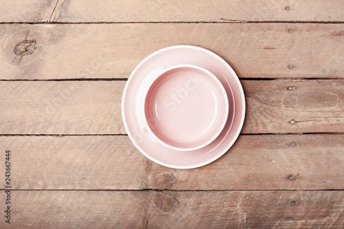Empty pink pastel colored plate and salad or soup bowl on grunge wood plank desk with copy space