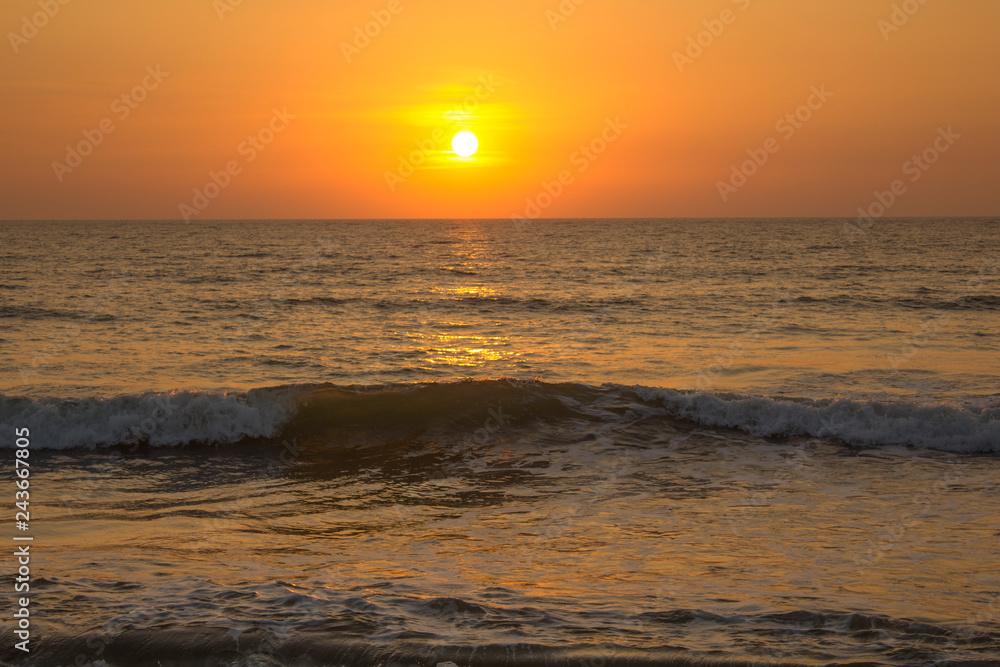 dark sea wave against a gray pink sky of sunset and yellow sun