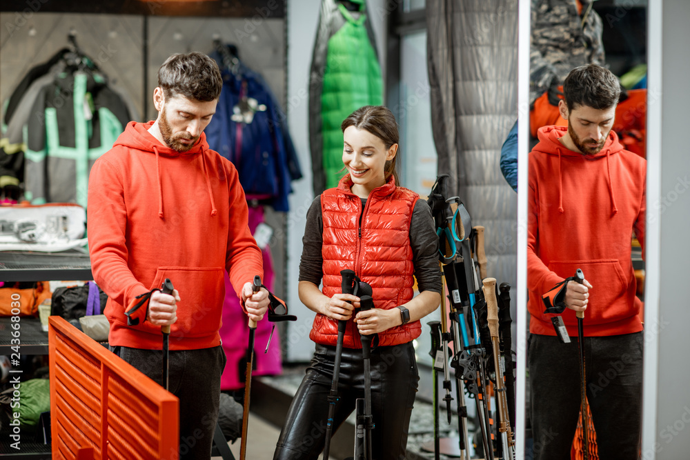 Man and woman choosing traveling equipment looking on the hiking sticks in the shop