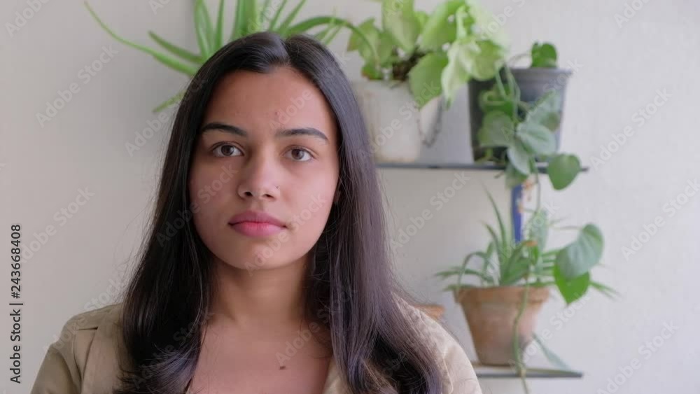 Attractive Indian woman nods her head ever so slightly listening to someone off camera with green plants in the background Attractive Indian woman nods her head ever so slightly listening to someone off camera with green plants in the background