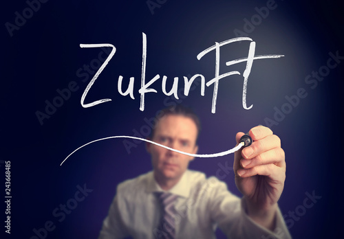 A businessman writing a Future "Zukunft" concept in German with a white pen on a clear screen.
