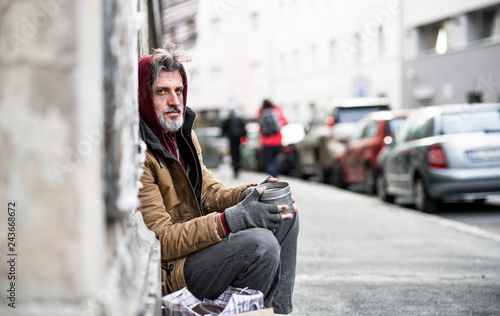 Homeless beggar man sitting outdoors in city asking for money donation.
