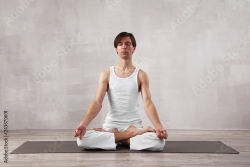 Young man in white clothes doing yoga in living room