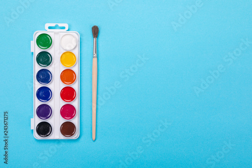 Watercolor paints and brush in white box, isolated on blue background