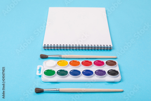 Set of aquarelle paints with brushes and album for painting isolated on blue background