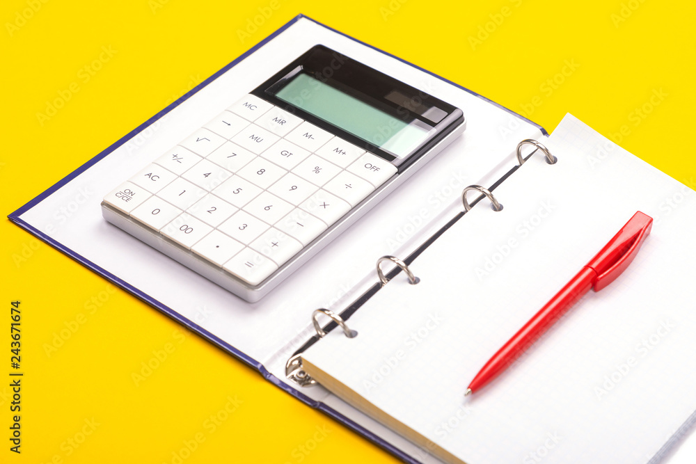 Top view of working space table with calculator, notebook and pen isolated on yellow background Top view of working space table with calculator, notebook and pen isolated on yellow background