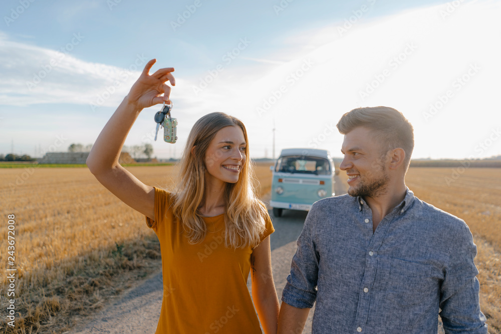 Young couple with car key on dirt track at camper van in rural landscape Young couple with car key on dirt track at camper van in rural landscape