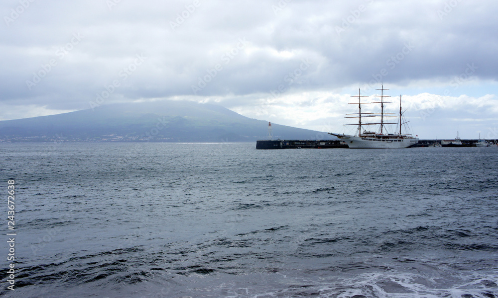 Three-masted sailing ship against the backdrop of the hidden in the clouds Pico volcano.Azores.