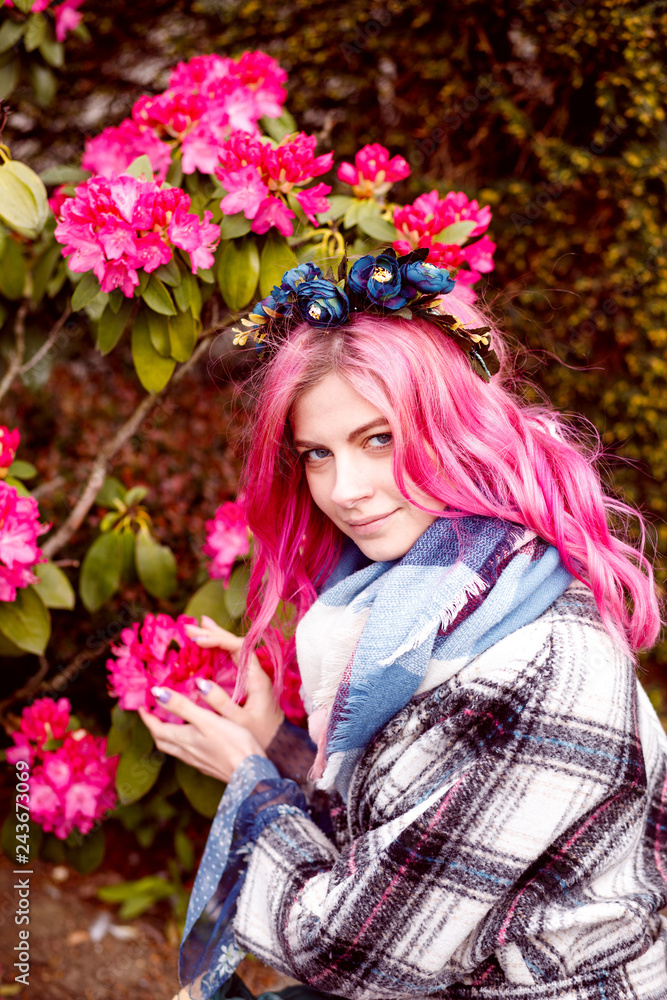 Fototapeta premium portrait of a beautiful girl with pink hair standing near pink flowers.