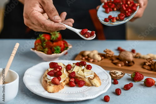 Sweet sandwiches with strawberries, cheese, camembert, brie, nuts and honey on the whole grain bread bruschetta cooking by chef hand on light background. Food recipe