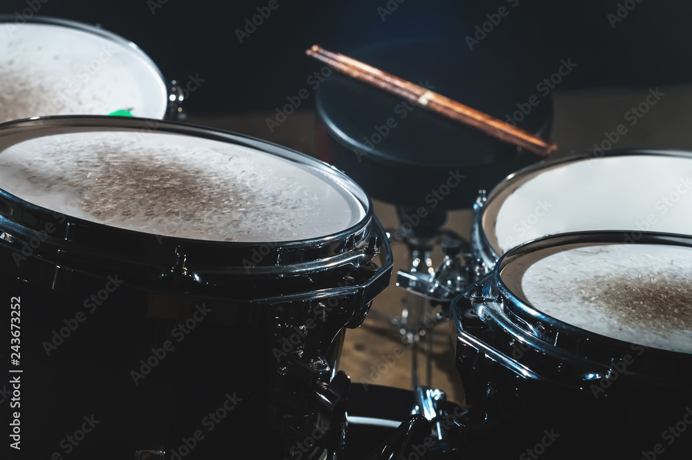 Closeup view of a drum set and Drumsticks in a dark studio. Black drum barrels with chrome trim. The concept of live performances Closeup view of a drum set and Drumsticks in a dark studio. Black drum barrels with chrome trim. The concept of live performances