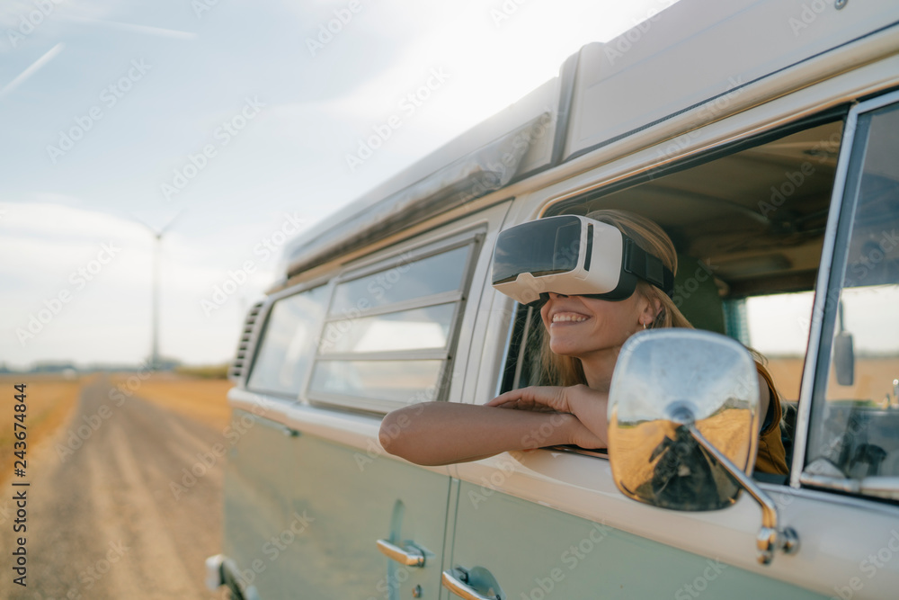 Smiling woman wearing VR glasses leaning out of window of a camper van Smiling woman wearing VR glasses leaning out of window of a camper van