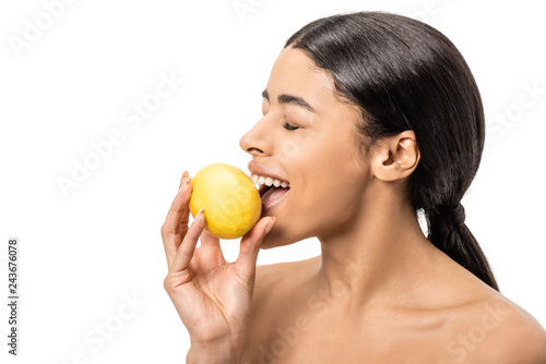 smiling naked african american girl with closed eyes biting lemon isolated on white